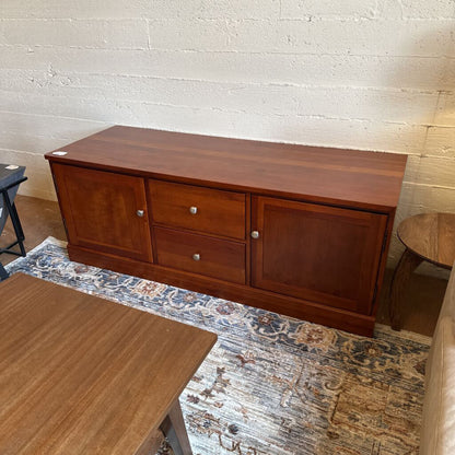 Wooden sideboard in a room with a textured wall and rug.