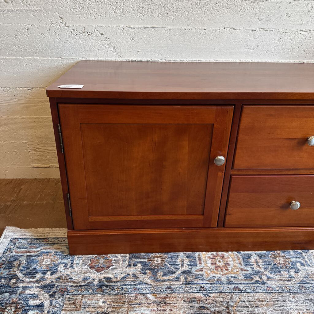 Wooden dresser with a cabinet and two drawers on a patterned rug.