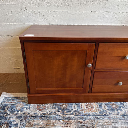 Wooden dresser with a cabinet and two drawers on a patterned rug.