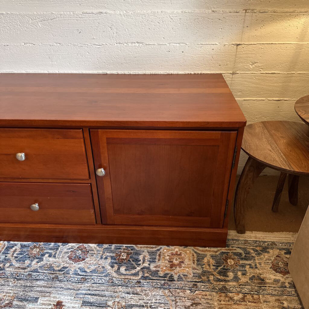 Wooden sideboard against a textured wall with a patterned rug on the floor.