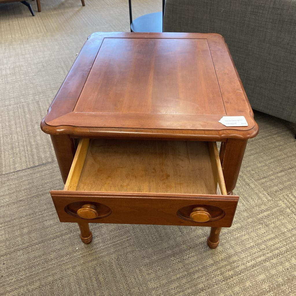 Wooden side table with a drawer on a carpeted floor
