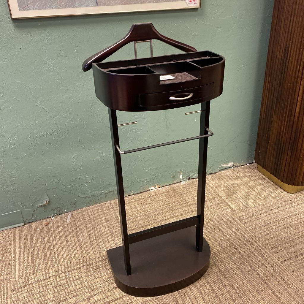 Dark wood valet stand with hanger and tray against a green wall.