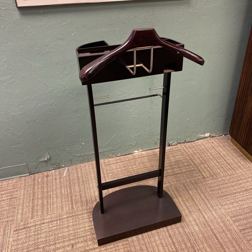 Vest stand with a wooden hanger on a textured floor against a green wall.