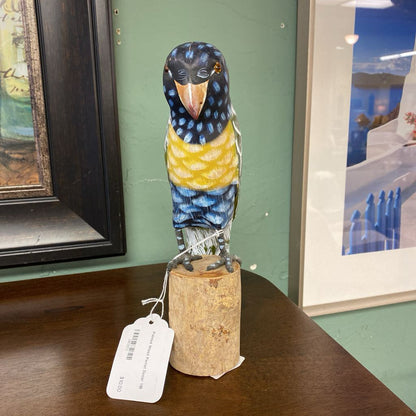 Decorative bird figurine on a cork base with a tag, displayed against a green wall with framed pictures.