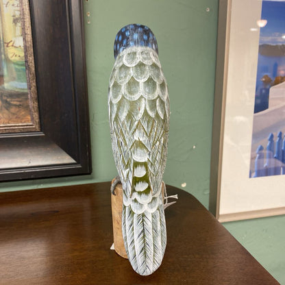 Decorative vase with feather design on a wooden surface, framed pictures in the background