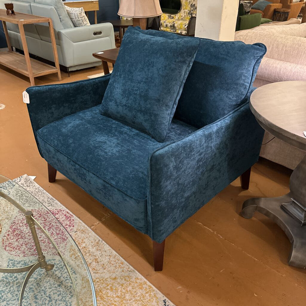 Blue velvet armchair in a showroom setting with other furniture.