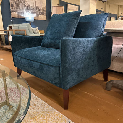 Blue velvet armchair in a showroom setting with other furniture.