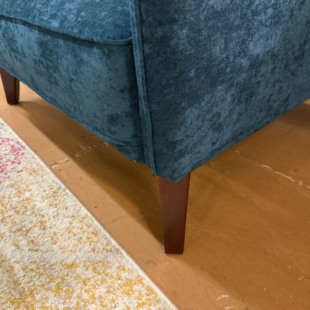 Close-up of a blue upholstered chair with wooden legs on a brown floor.