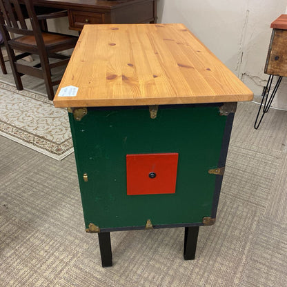 Wooden table with a green base and red square on a carpeted floor.