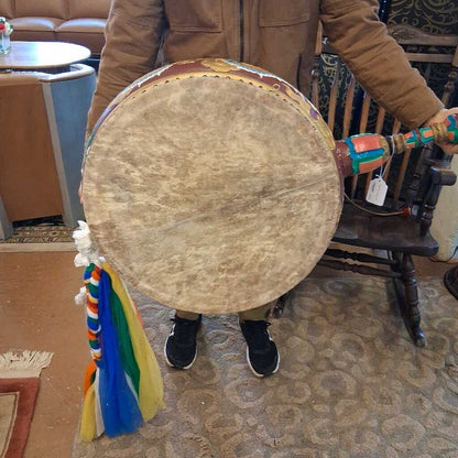 Person holding a large wooden drum with colorful decorations indoors.