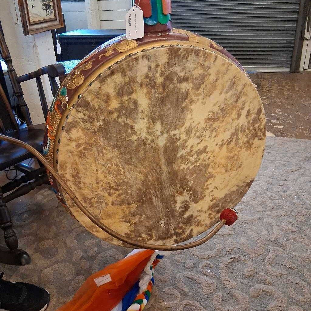 Vintage-style drum held by a person indoors with a chair and table in the background.