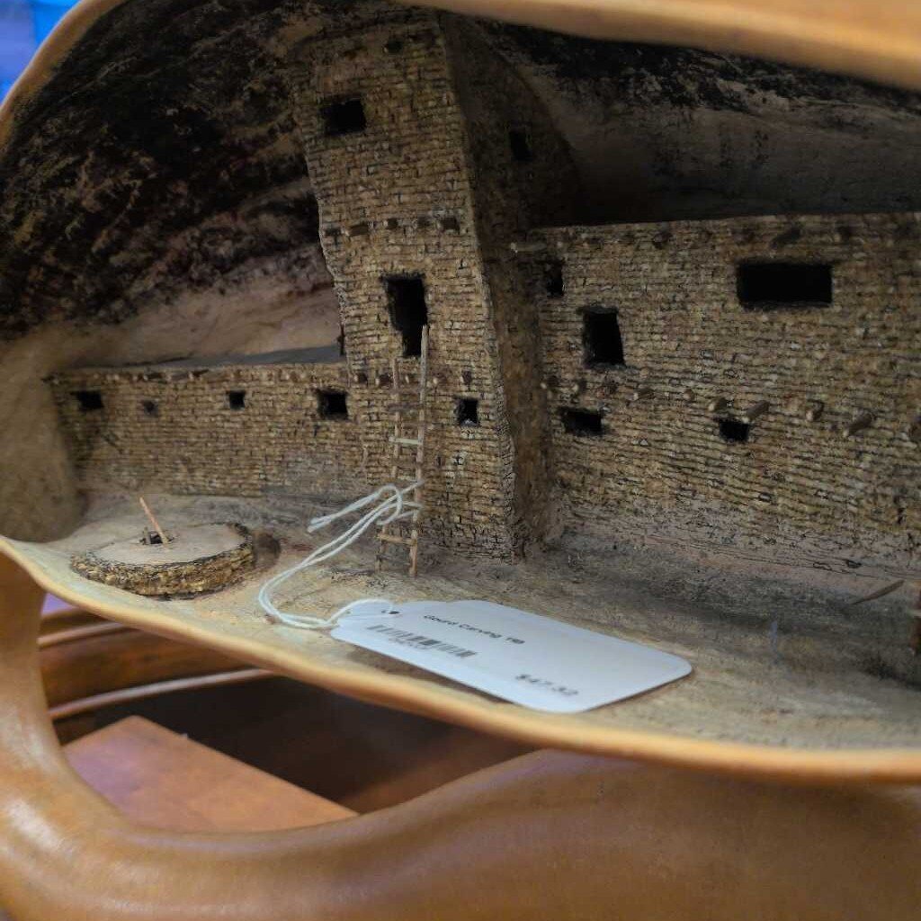 Model of a stone building inside a wooden bowl with a tag attached.