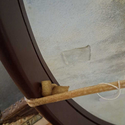 Close-up of a round mirror with a wooden frame and a stick leaning against it.