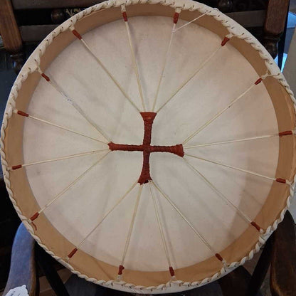 Close-up of a round drum with a white skin and red cross pattern on a wooden stand.