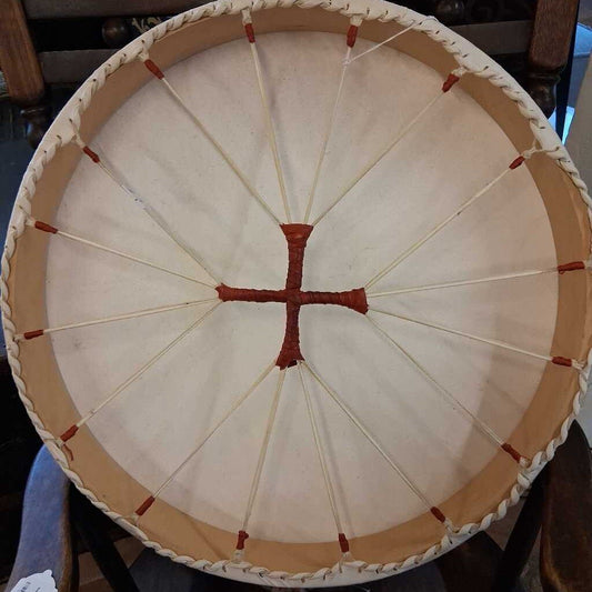 Close-up of a round drum with a white skin and red cross pattern on a wooden stand.