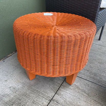 Round orange wicker table on a concrete floor with a chair in the background.