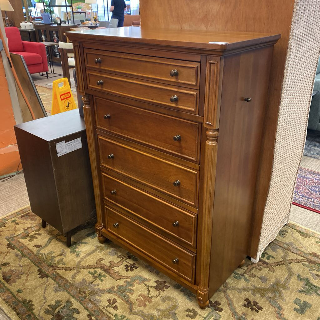 Wooden dresser with multiple drawers on a patterned rug in a store setting.
