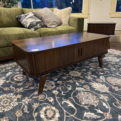 Wooden coffee table in a living room with a green sofa and patterned rug.