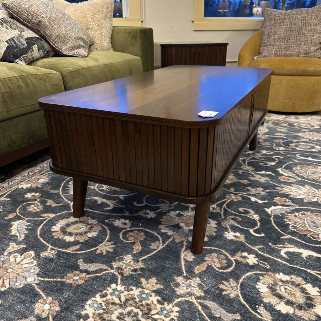Wooden coffee table in a living room with a patterned rug and couches.