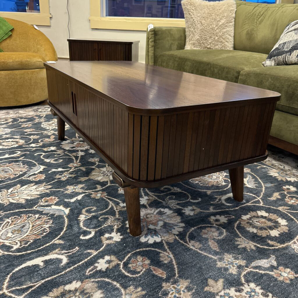 Wooden coffee table in a living room with a green sofa and patterned rug.