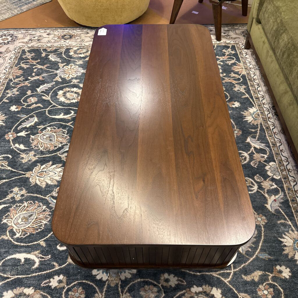 Wooden coffee table on a patterned rug with a green couch and chair in the background.