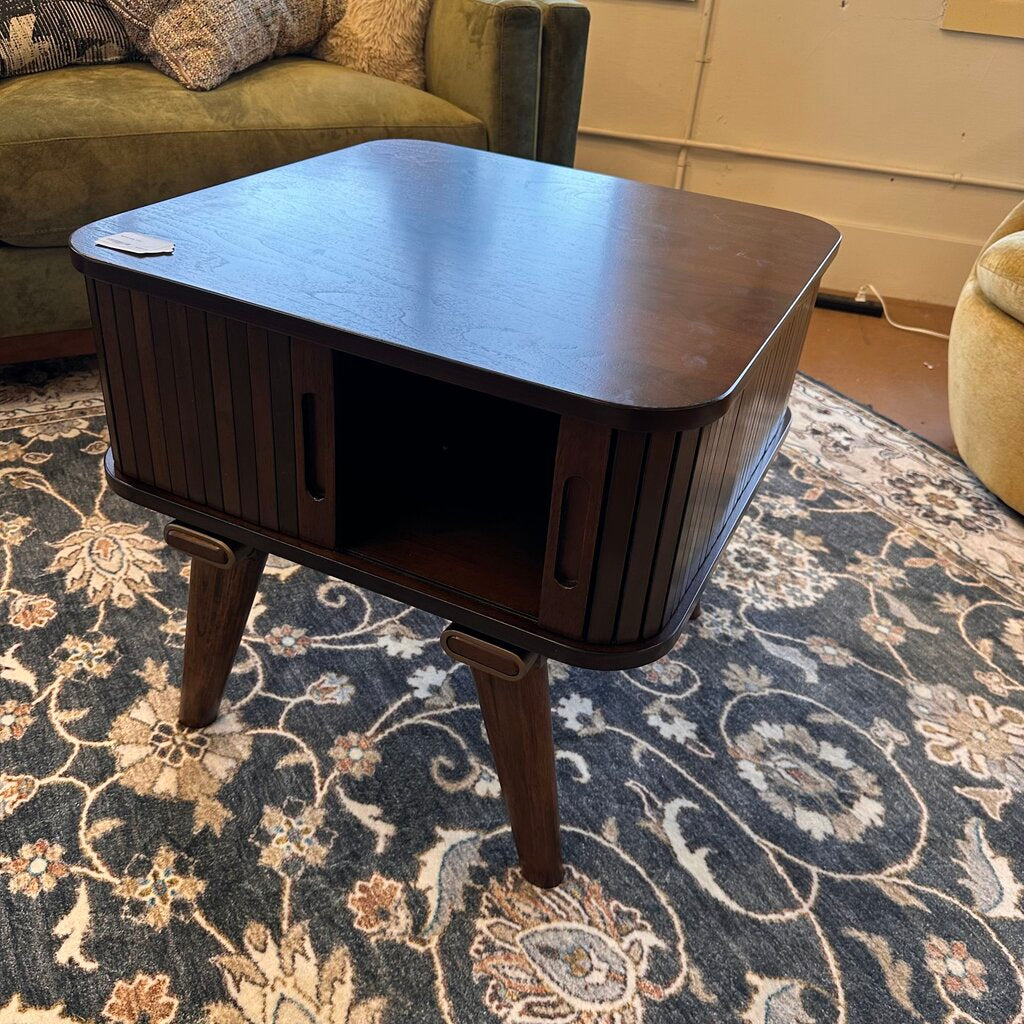 Dark wooden side table in a living room setting with a floral-patterned rug.