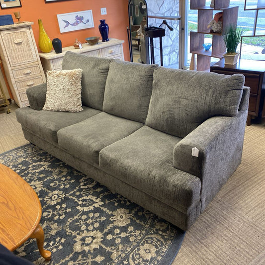 Gray sofa with a textured pillow on a patterned rug in a room with furniture and decor.