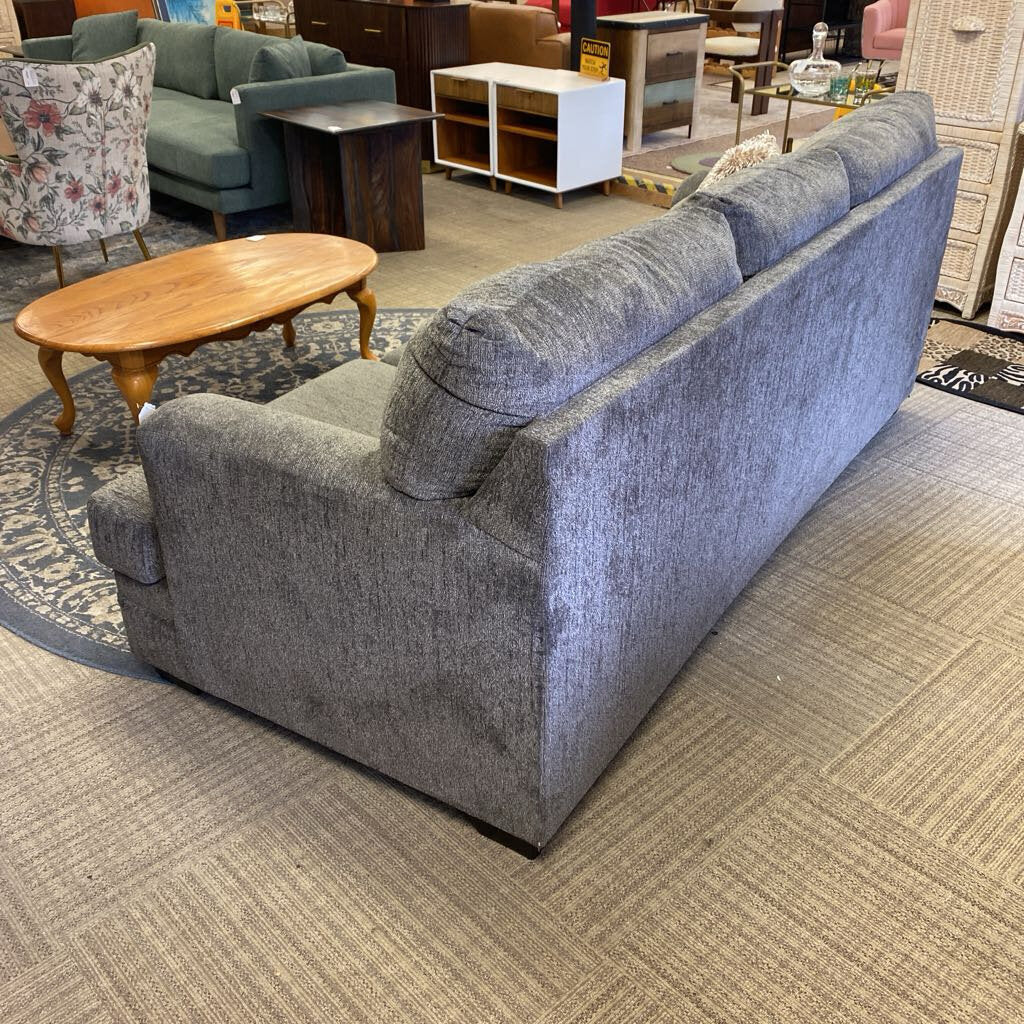 Gray sofa in a furniture store setting with other furniture items around.
