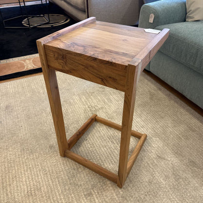 Wooden side table in a living room setting with a sofa and rug.