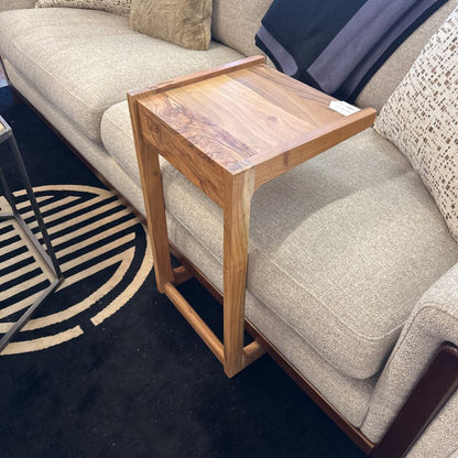 Wooden side table next to a beige sofa on a dark blue rug with a circular pattern.