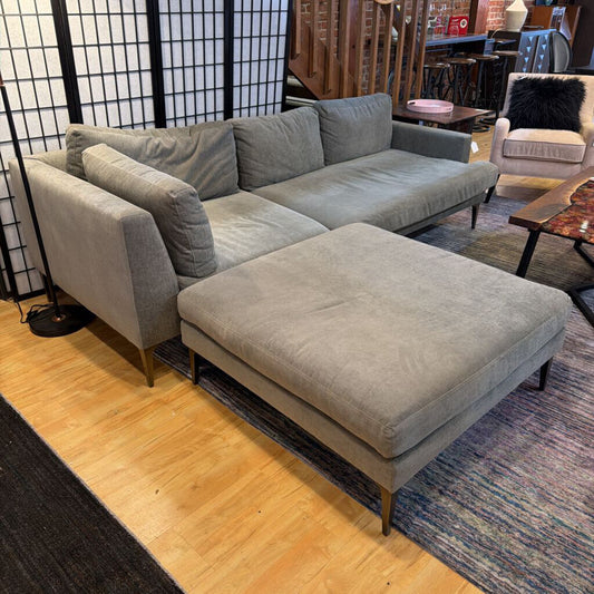 Gray sectional sofa with ottoman in a room with wooden floor and decorative elements.