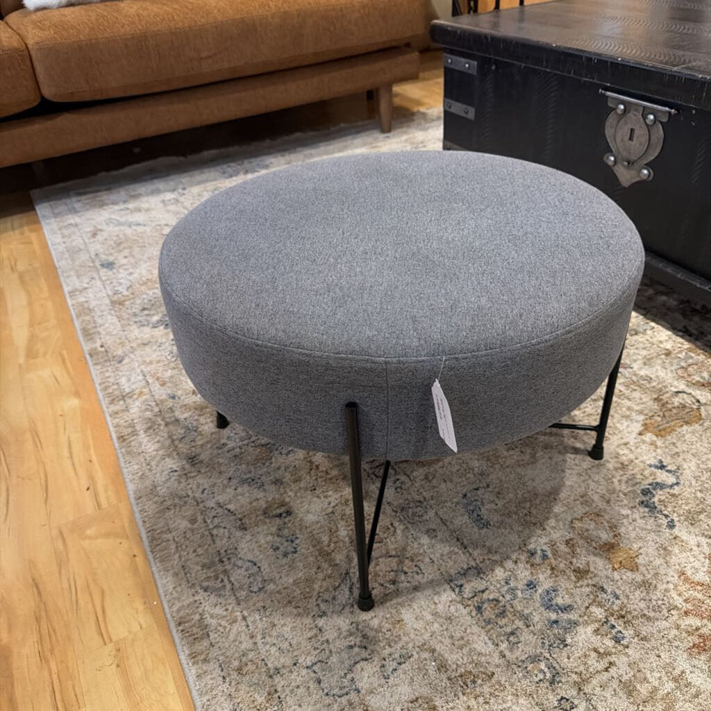 Gray ottoman with a price tag on a patterned rug in a room setting.
