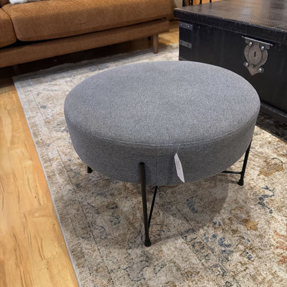 Gray ottoman with a price tag on a patterned rug in a room setting.
