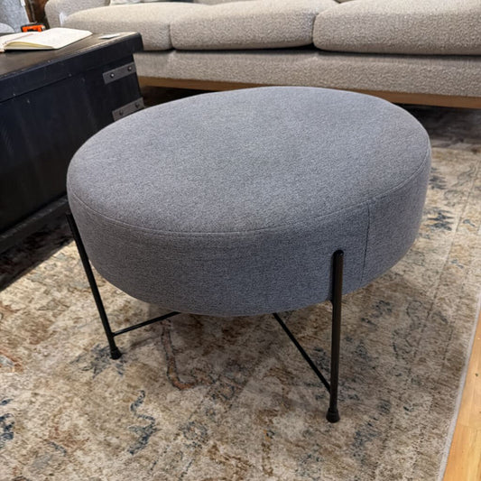 Gray ottoman with metal legs on a patterned rug in a living room setting.