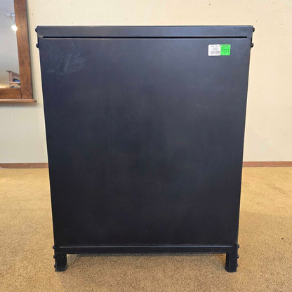 Black refrigerator on a beige carpeted floor with a white wall in the background