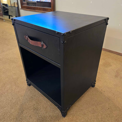 Black metal nightstand with a drawer on a beige carpeted floor.
