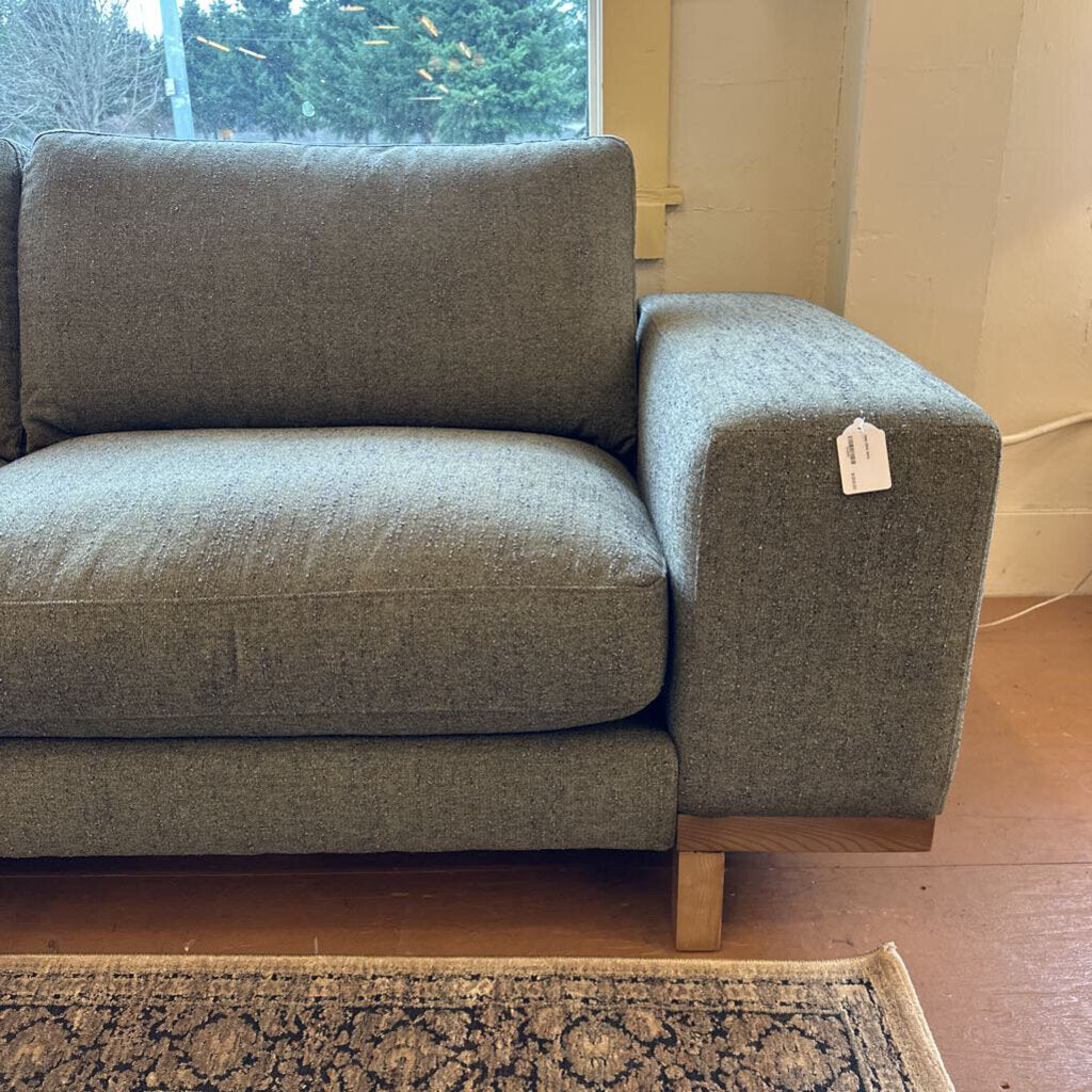 Gray sofa with a price tag in a room with a window and wooden floor.