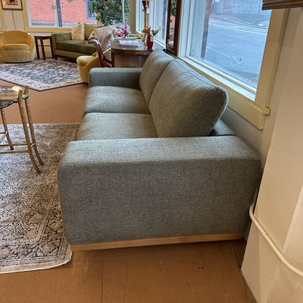 Gray sectional sofa in a living room with wooden floor and large window.