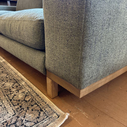 Gray upholstered sofa with wooden legs on a wooden floor.