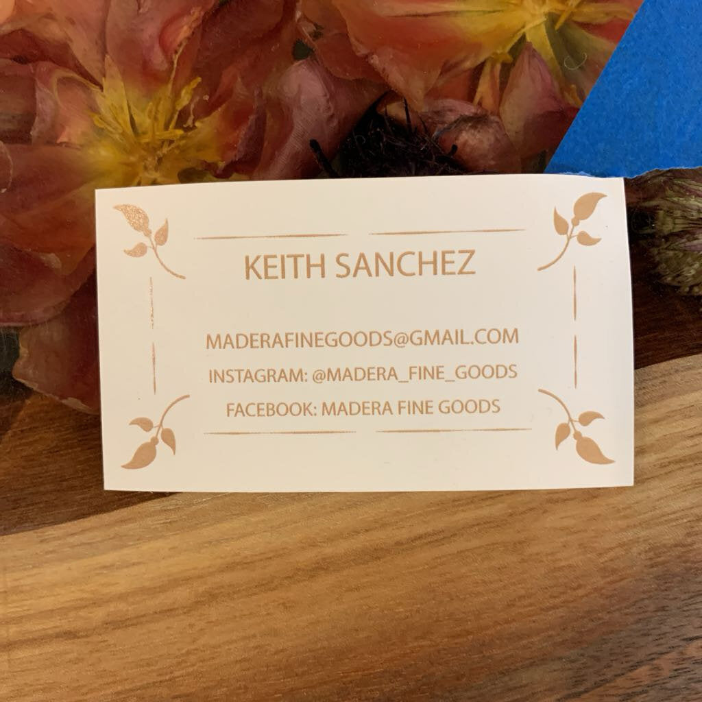 Business card with contact information on a wooden surface with flowers in the background