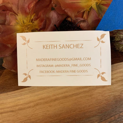 Business card with contact information on a wooden surface with flowers in the background
