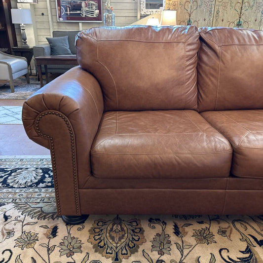 Brown leather sofa in a living room setting with a patterned rug.