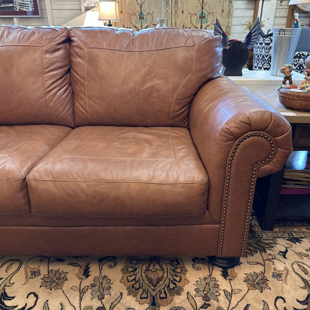 Brown leather sofa in a living room setting with a patterned rug.