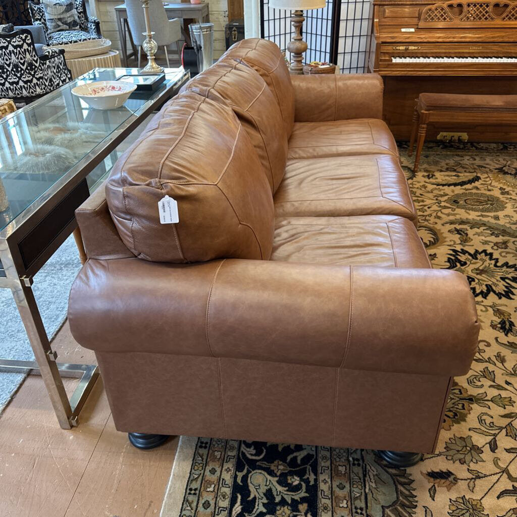 Brown leather sofa in a room with a glass table, chairs, and a piano.