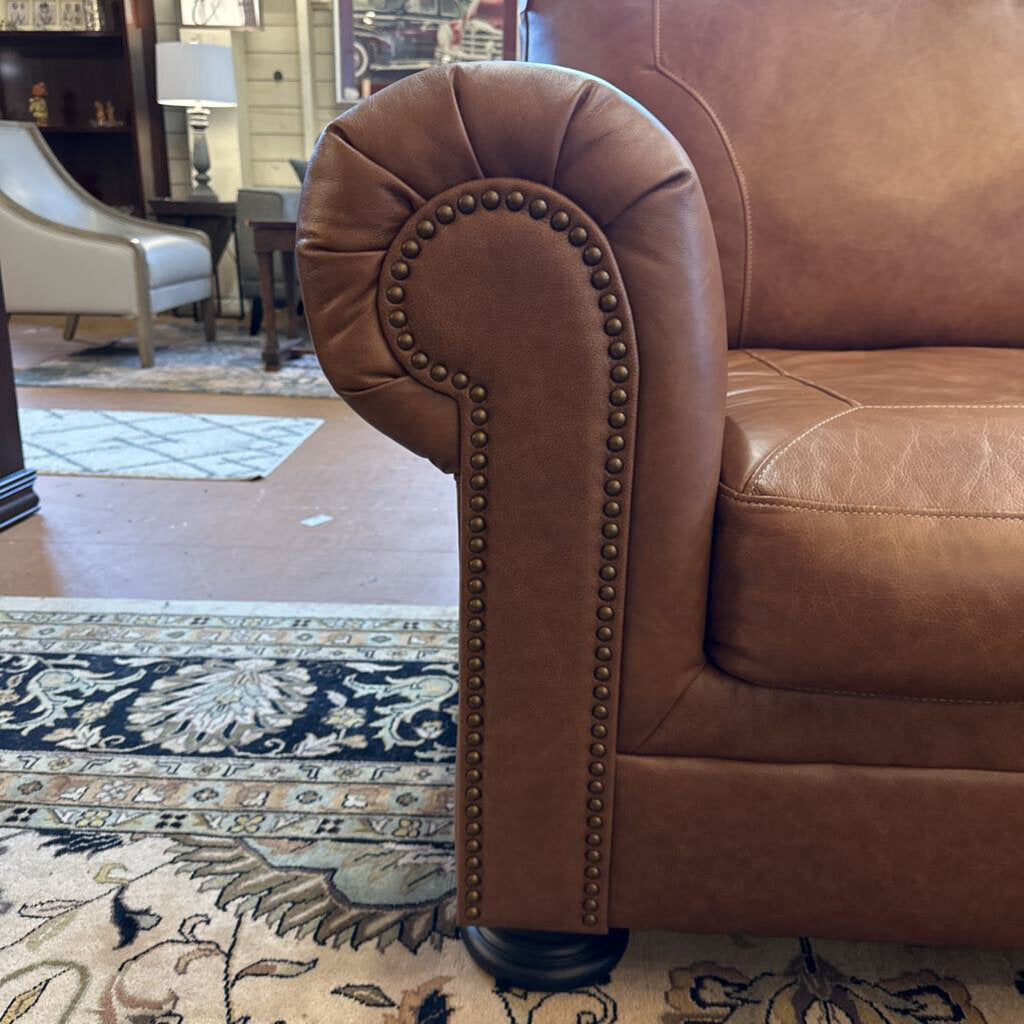 Brown leather sofa with nailhead trim in a room with a rug and furniture.