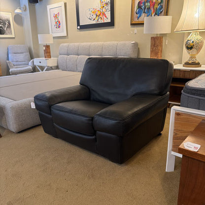 Black leather recliner chair in a furniture store with gray sofa and decorative items in the background.