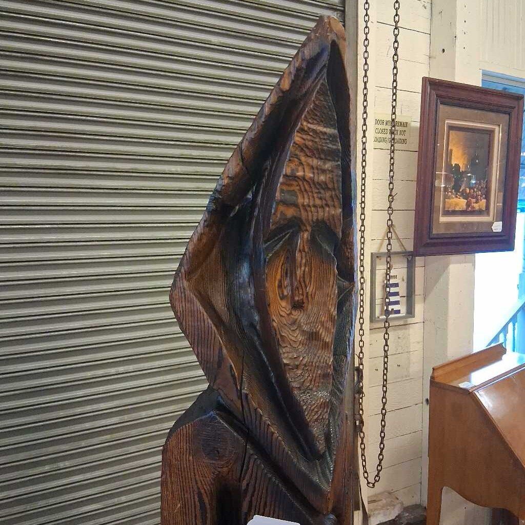 Wooden sculpture hanging on a wall with a metal shutter in the background