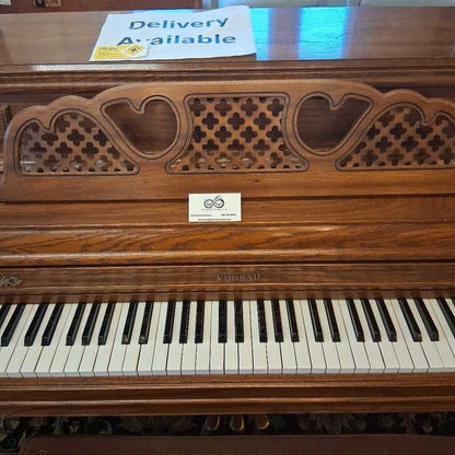 Wooden piano with decorative front panel and 'Delivery Available' sign.