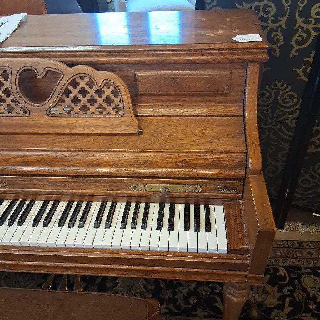 Wooden piano with decorative front panel in a room with patterned wallpaper.
