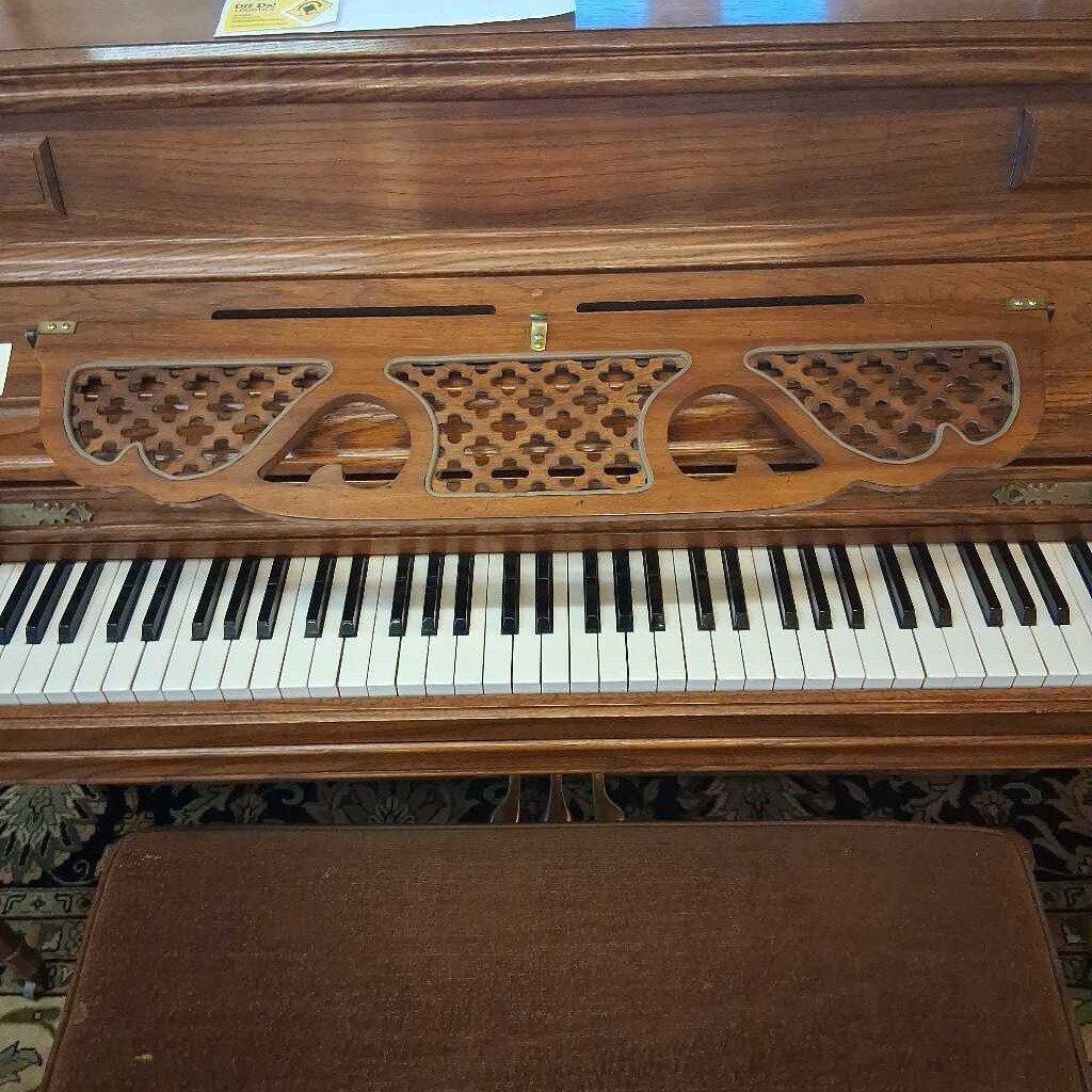 Wooden piano with decorative carvings and a brown bench in front